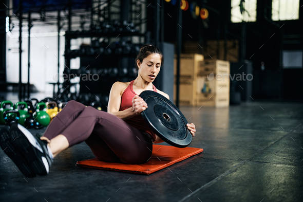 Female athlete doing sit ups with weight plate while working out in a gym